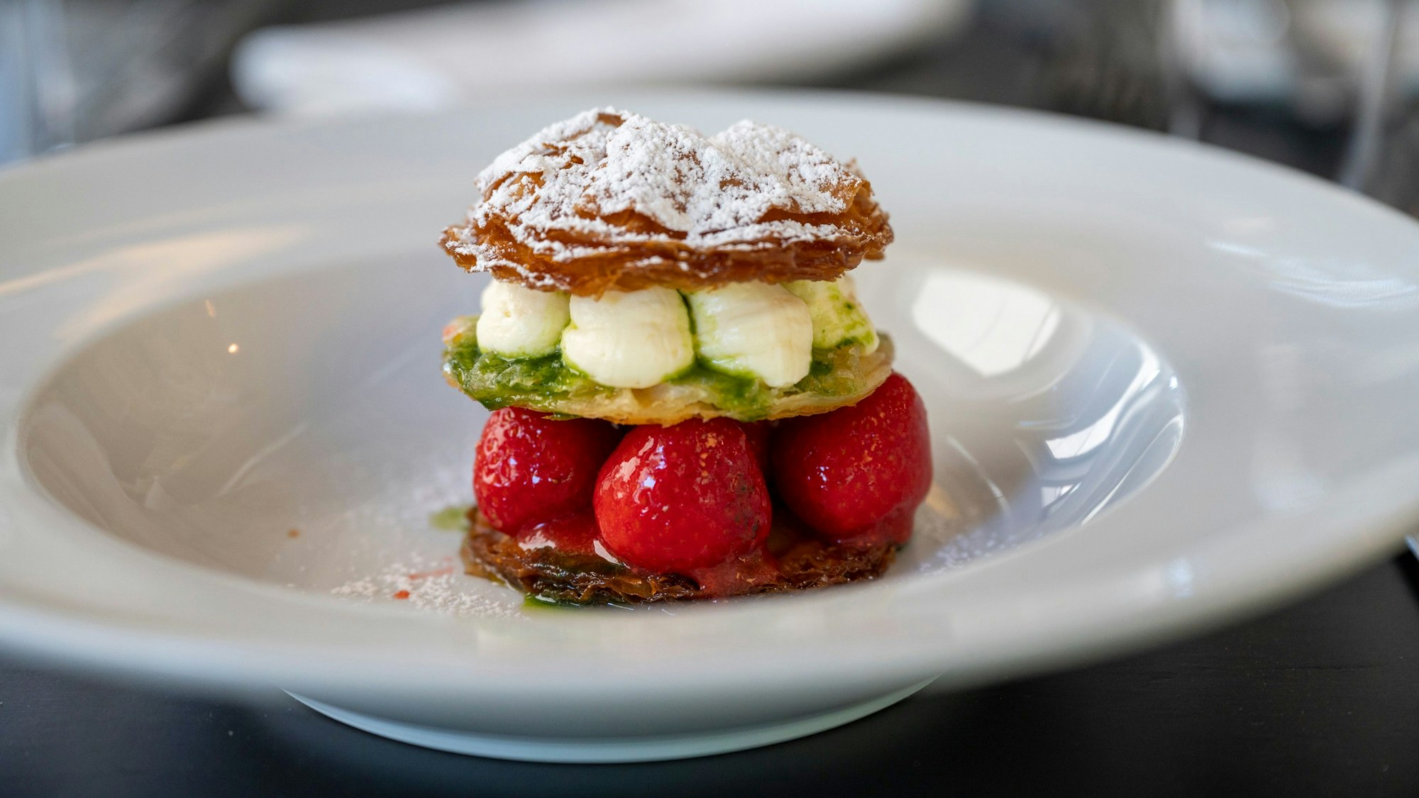 Yufka-Teig-Kreise, Erdbeeren, weiße Schokoladenmousse und Thymiansauce liegen auf einem Teller.