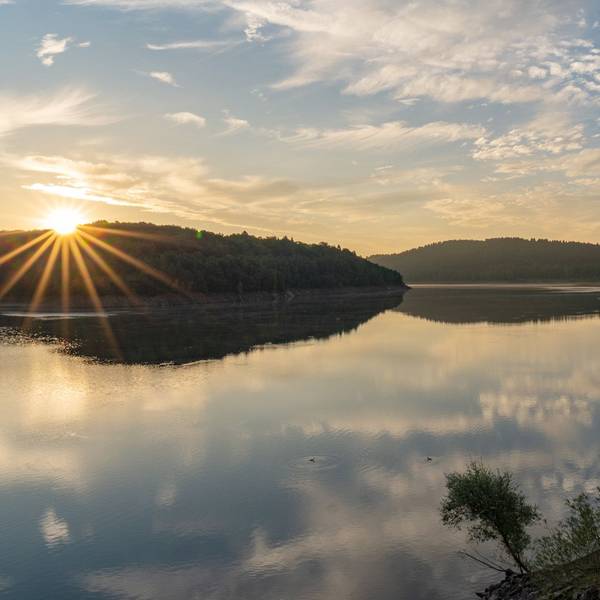 Die Sonne steht über den Bäumen am Ufer der Großen Dhünn-Talsperre.