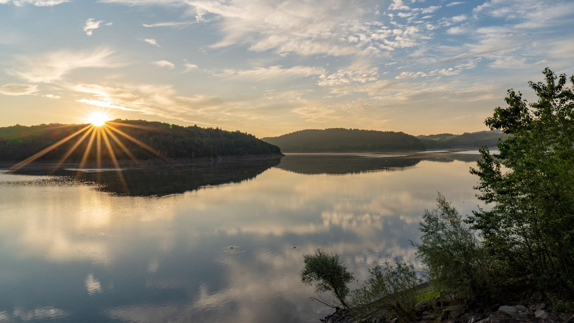 Die Sonne steht über den Bäumen am Ufer der Großen Dhünn-Talsperre.