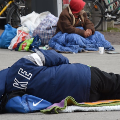 Das Foto zeigt einen obdachlosen Menschen, der auf dem Asphalt liegt.