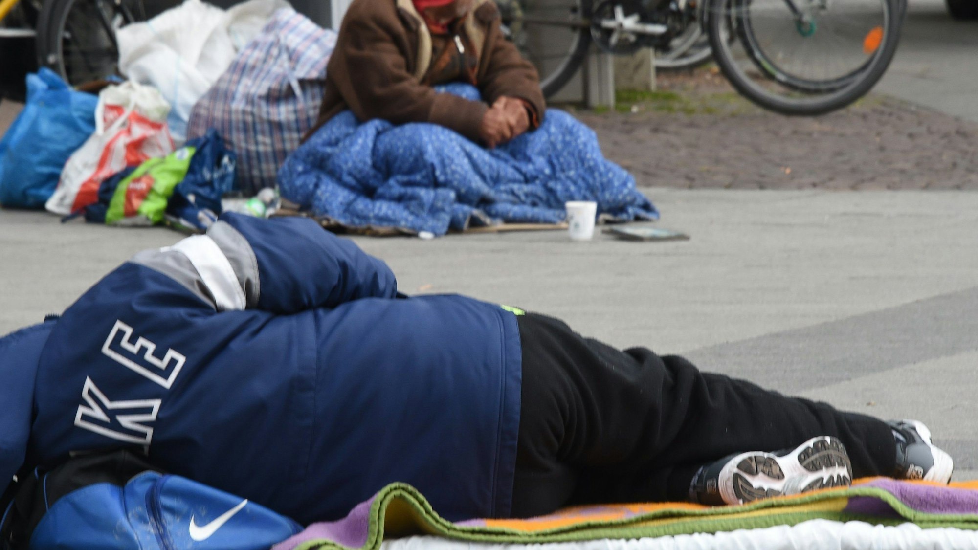 Das Foto zeigt einen obdachlosen Menschen, der auf dem Asphalt liegt.