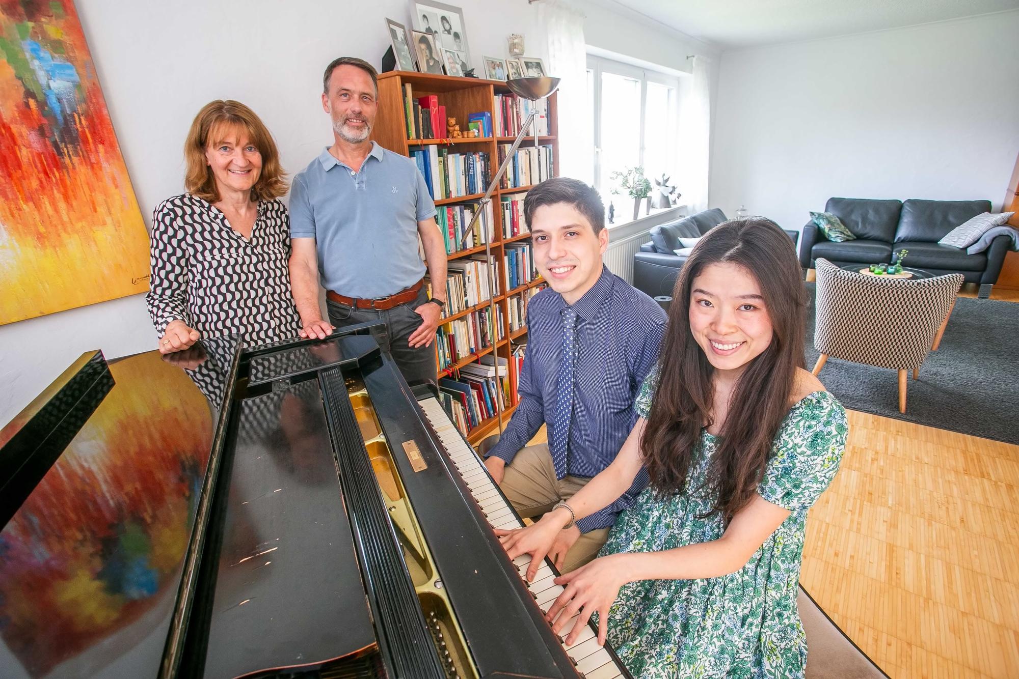 Die beiden Pianisten MimiZhang und David Mach sitzen an einem Klavier, neben dem Instrument stehen Marie-Therese und bernd Wegerhoff, die beiden Gasteltern aus Marienheide.