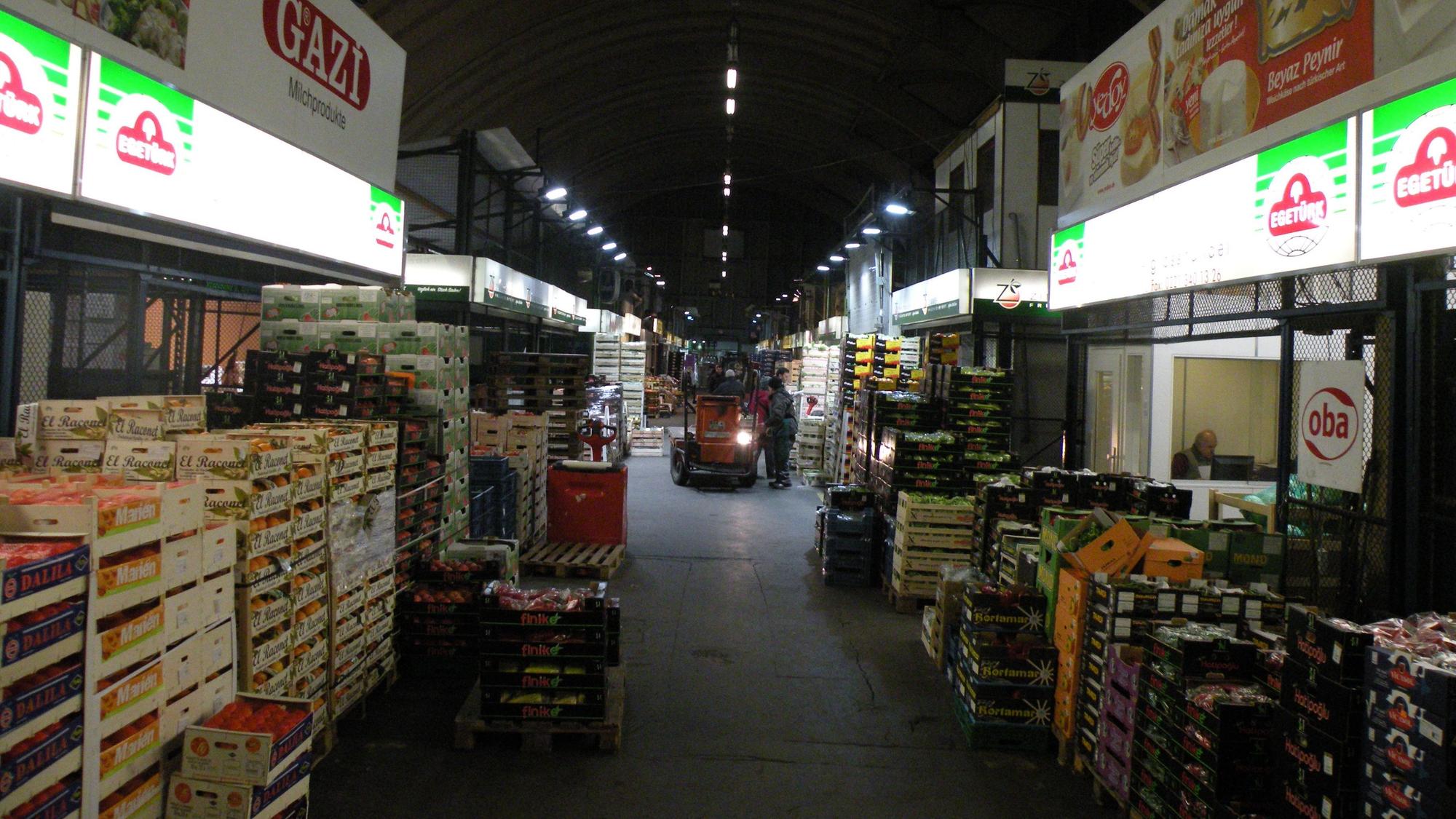 Große Körbe voller Obst stehen aufeinander gestapelt am Rand der Fahrgasse durch die Halle des Kölner Großmarkts.
