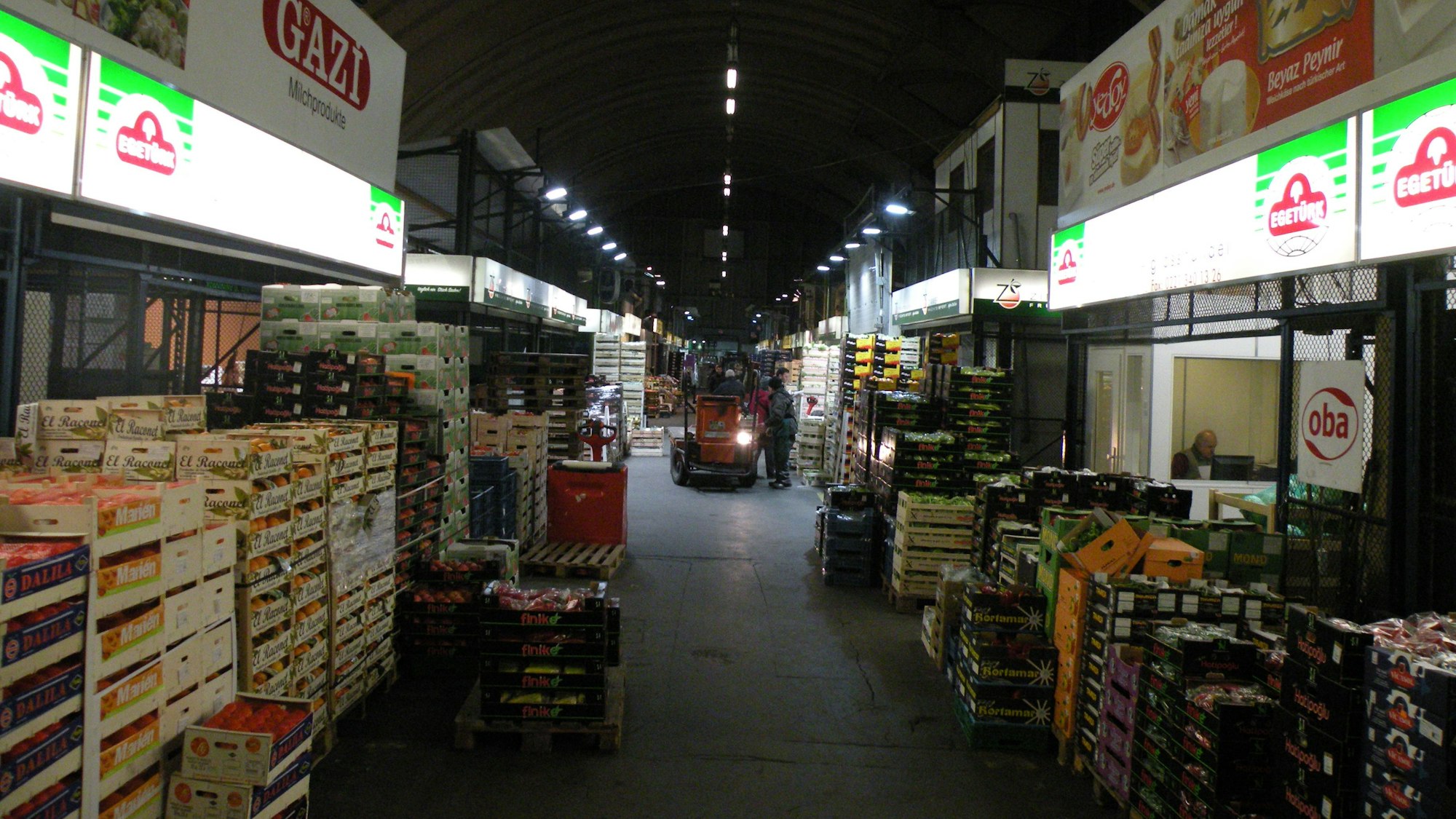 Große Körbe voller Obst stehen aufeinander gestapelt am Rand der Fahrgasse durch die Halle des Kölner Großmarkts.