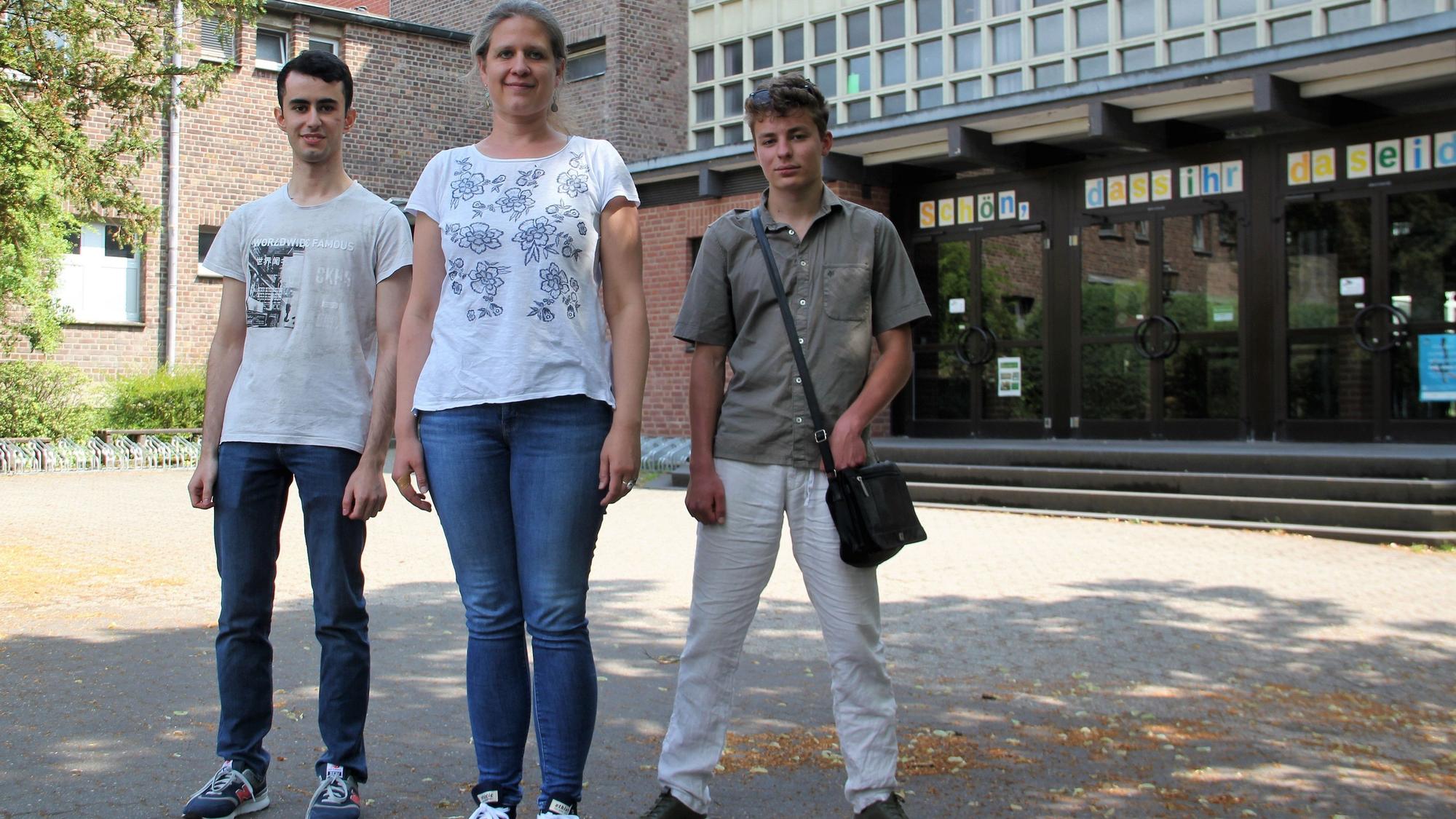 Zwei junge Männer stehen links und rechts von einer blonden Frau mit Pferdeschwanz.