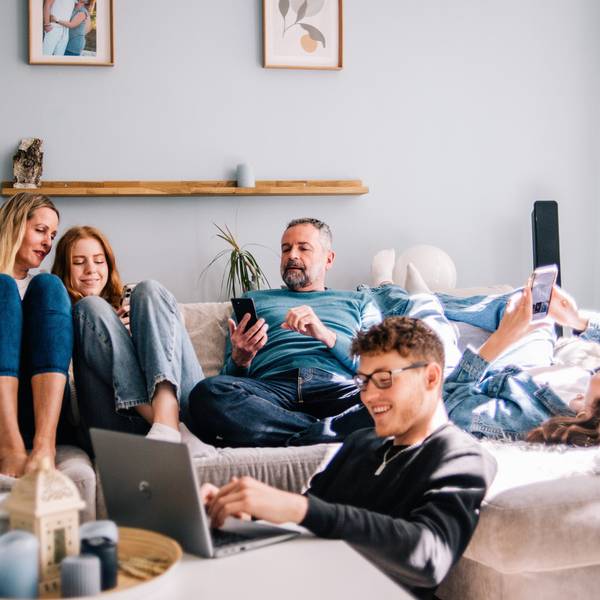 Eine Familie sitzt gemeinsam auf einer Couch. Davor sitzt ein Jugendlicher an einem Laptop.