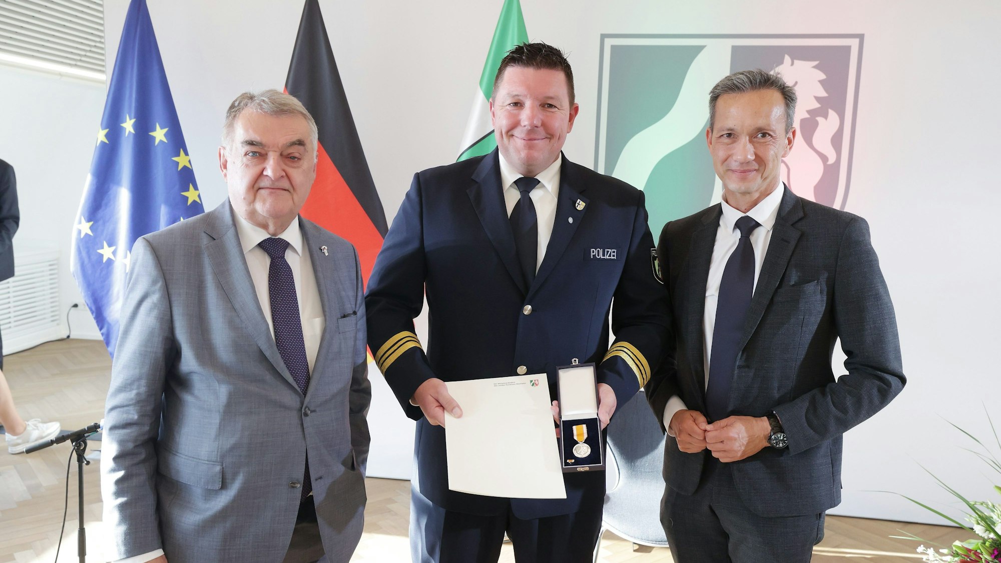 Patrick Reichelt (M), Polizeihauptkommissar aus Swisttal, steht neben Herbert Reul (CDU, l), Innenminister von Nordrhein-Westfalen, und Falk Schnabel, Polizeipräsident von Köln, bei der Verleihung der Rettungsmedaille des Landes Nordrhein-Westfalen.