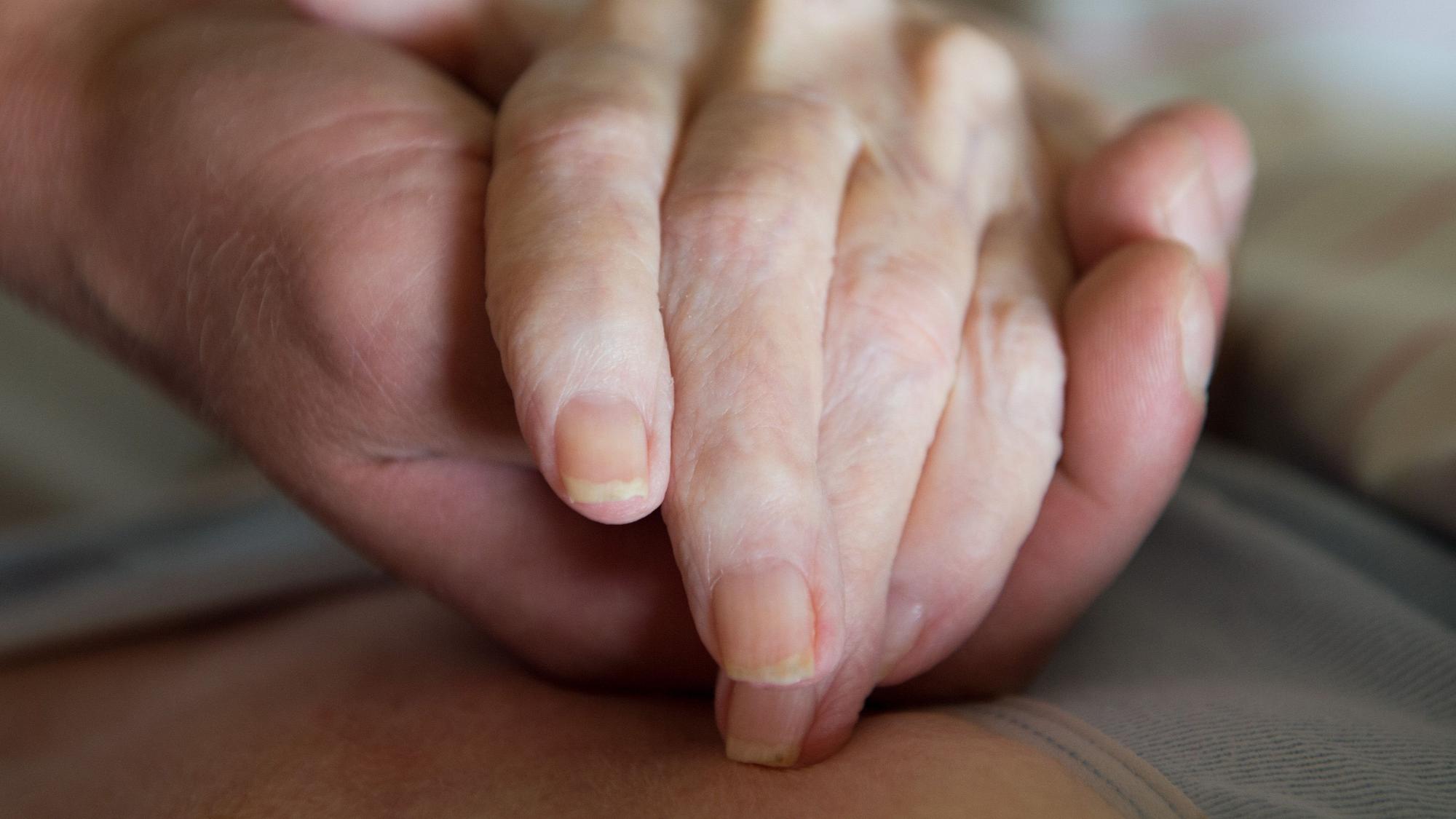 Eine Hand hält die knochige Hand eines älteren Menschen.
