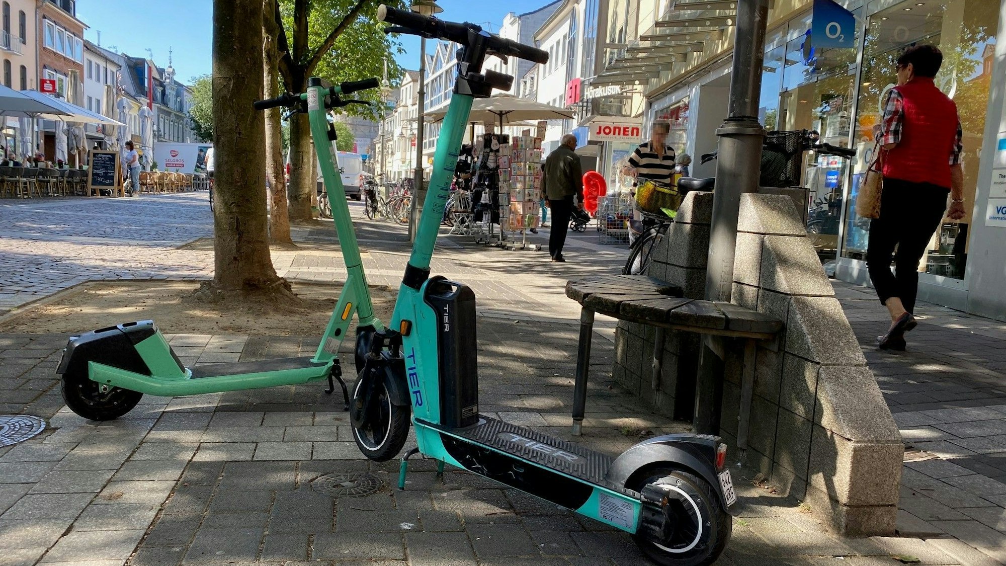 Zwei E-Scooter stehen in der Brühler Fußgängerzone, Passanten umkurven die kleinen Elektroflitzer.