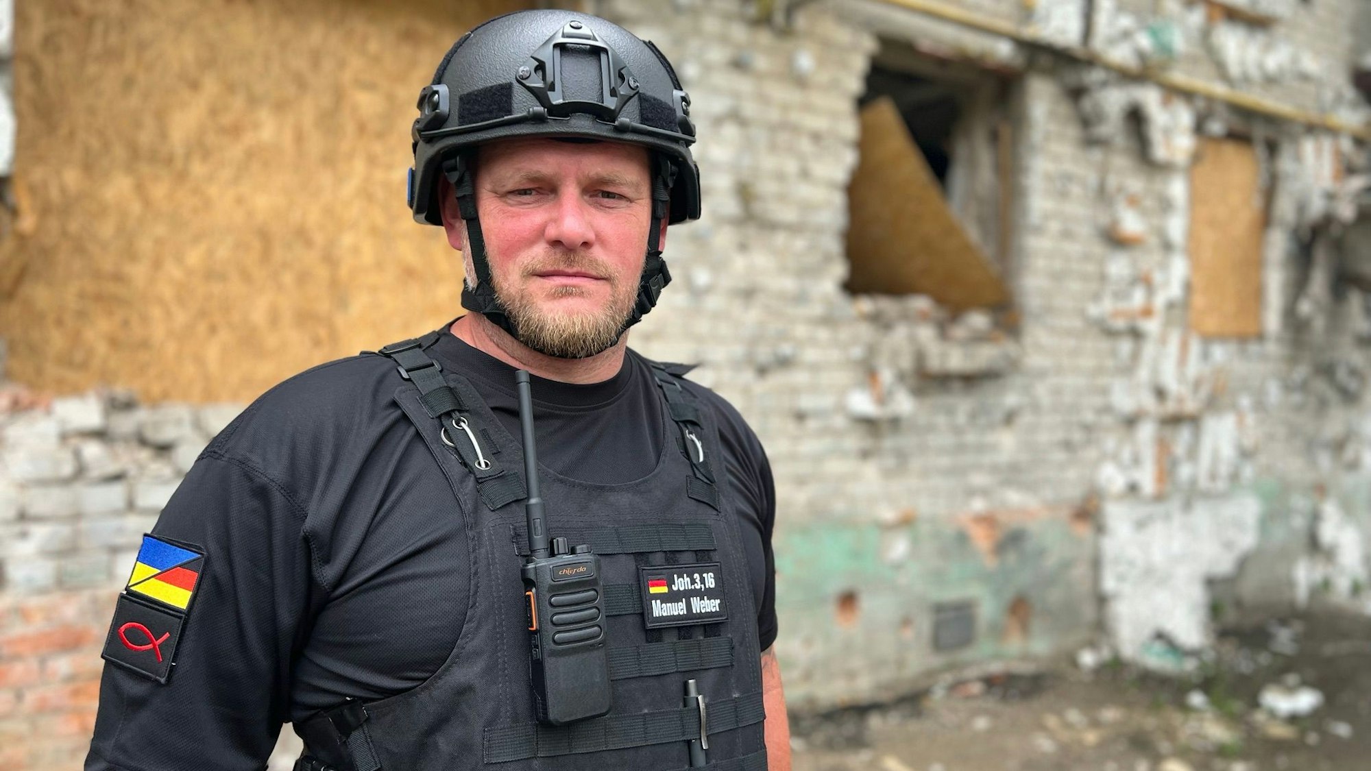Ein Mann mit Helm steht vor einer Kriegsruine.