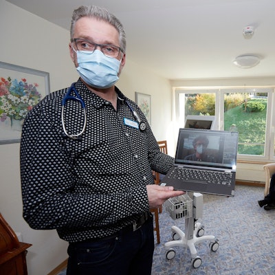 Pflegedienstleiter Arno Brauckmann hält ein Notebook in der Hand und demonstriert, was ein Arzt bei der Telemedizin sehen würde. Im Hintergrund sitzt eine Patientin.