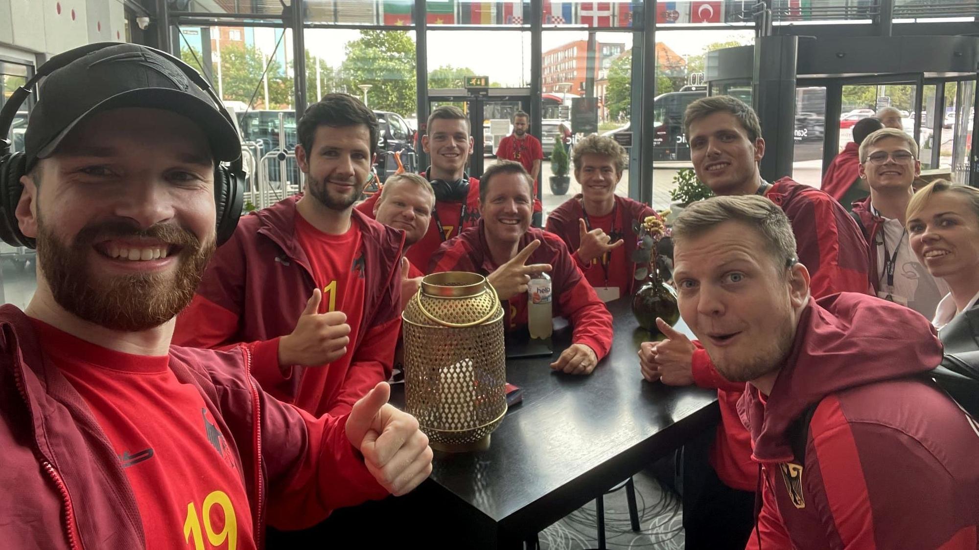 Dieses Selfie von Simon Schöller zeigt eine gut gelaunte Handball-Nationalmannschaft der Gehörlosen, die um einen Tisch versammelt sitzt.