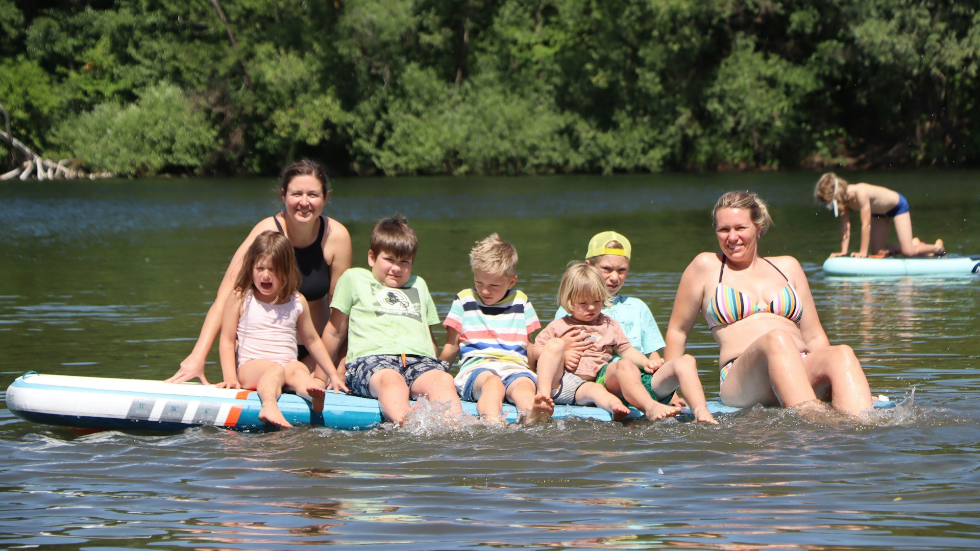 Frauen und Kinder auf einem Surfbrett im Wasser.