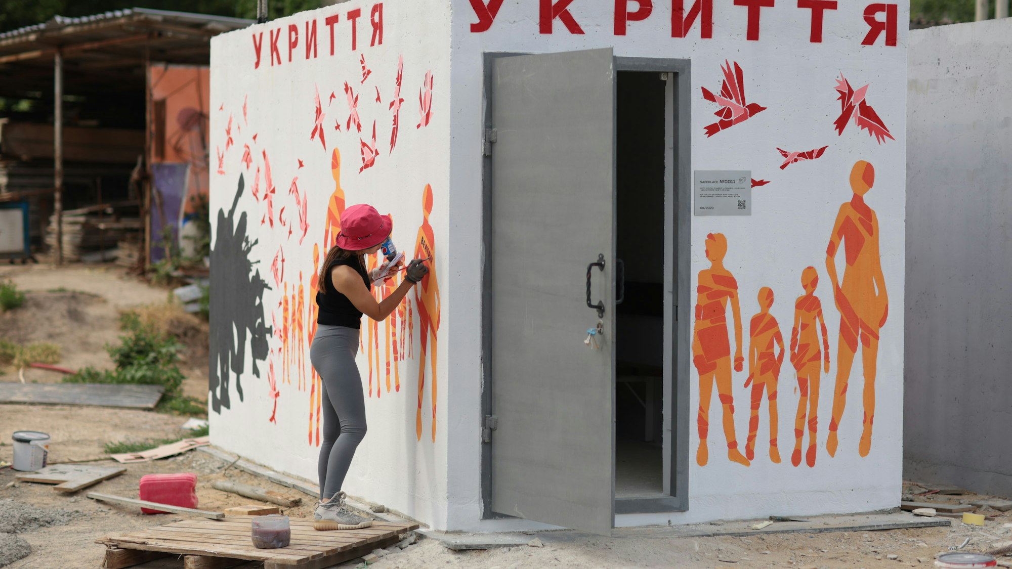 Eine Künstlerin zeichnet orangefarbene Figuren auf die weißen Wände des Bunkers.