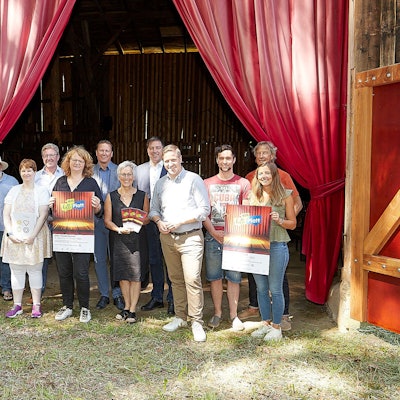 Eine Gruppe von Menschen steht vor einem roten Theatervorhang, einige halten Plakate in den Händen.