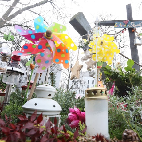 Auf einem bepflanzten Grab stehen bunte Windräder und weiße Grabkerzen.