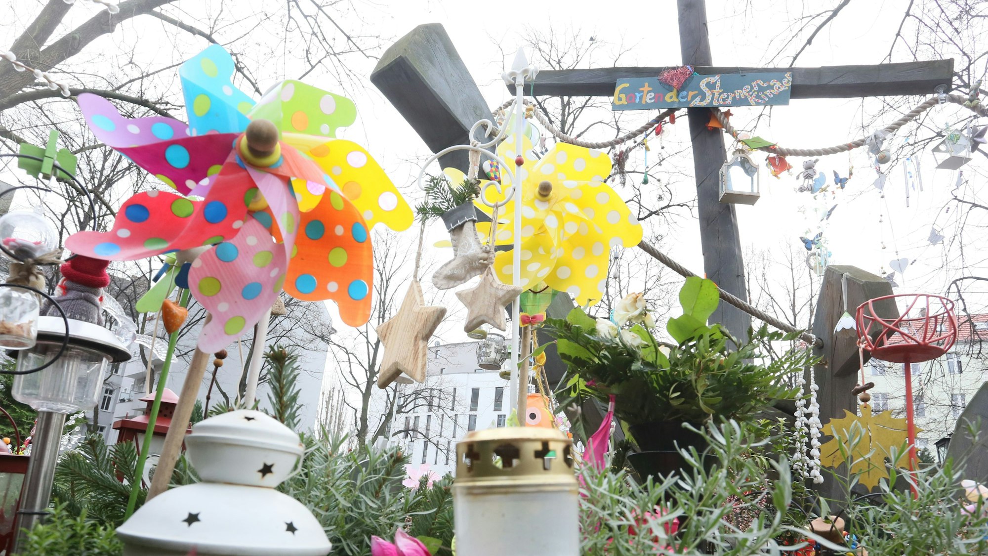 Auf einem bepflanzten Grab stehen bunte Windräder und weiße Grabkerzen.