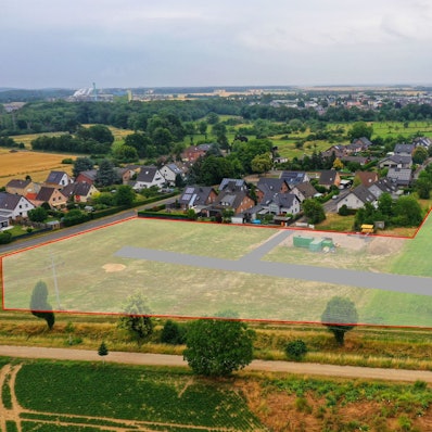Ein Luftbild zeigt ein paar Häuser. Auf den Wiesen davor ist eingezeichnet, wo das neue Baugebiet entstehen soll.