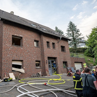 Feuerwehrleute stehen vor einem zweigeschossigen Klinkerhaus, davor liegen Schläuche.
