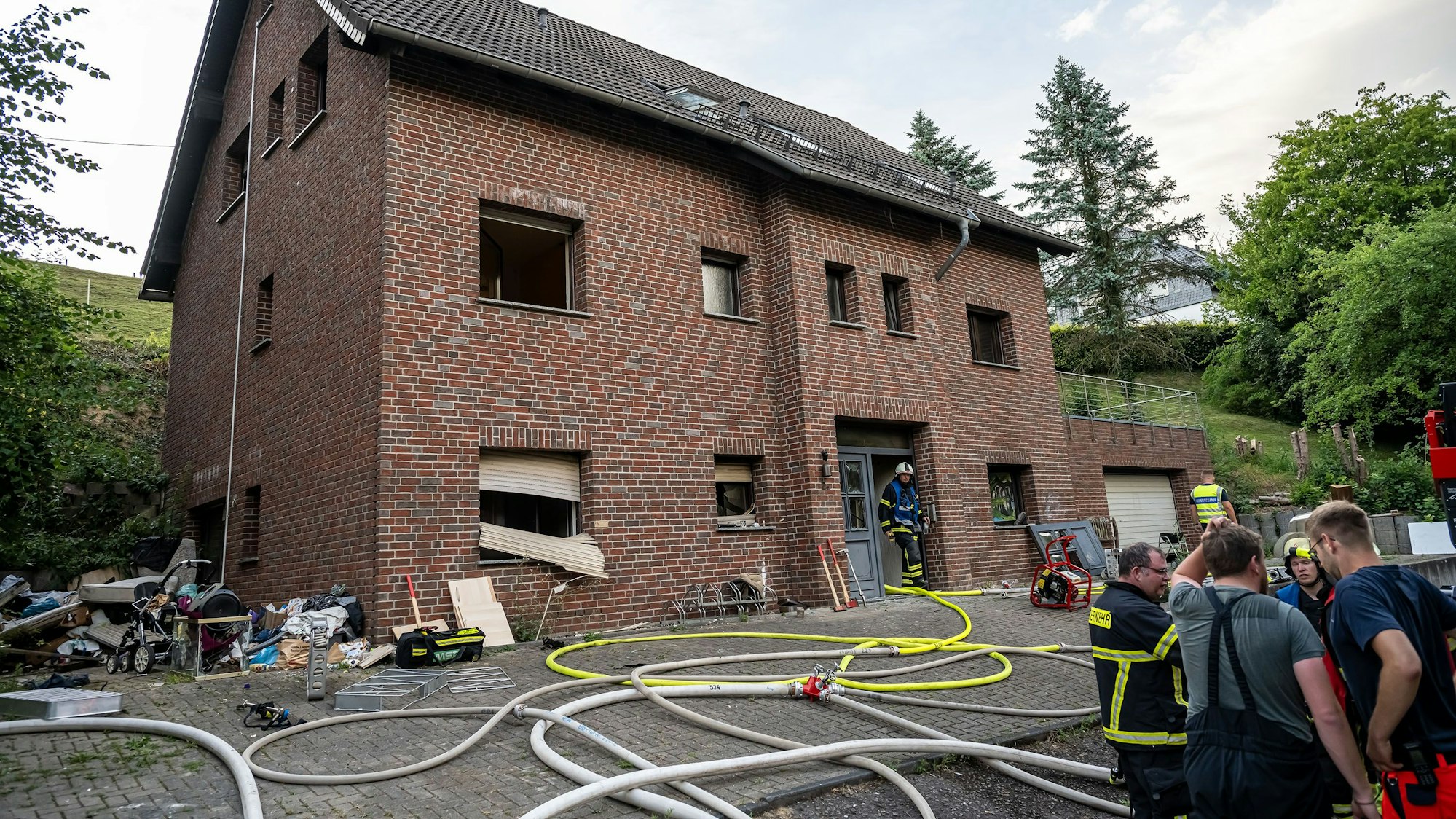 Feuerwehrleute stehen vor einem zweigeschossigen Klinkerhaus, davor liegen Schläuche.