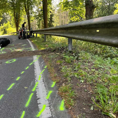 Ein Motorrad liegt nach einem Zusammenstoß auf dem Boden. Vor dem Zweirad wurden von der Polizei Unfallmarkierungen auf den Boden gesprüht.