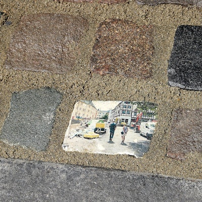 Das Bild zeigt mehrere Pflastersteine in Bad Münstereifel. Der Mittlere ist mit einem Motiv aus den Tagen nach der Flutkatastrophe bedruckt.