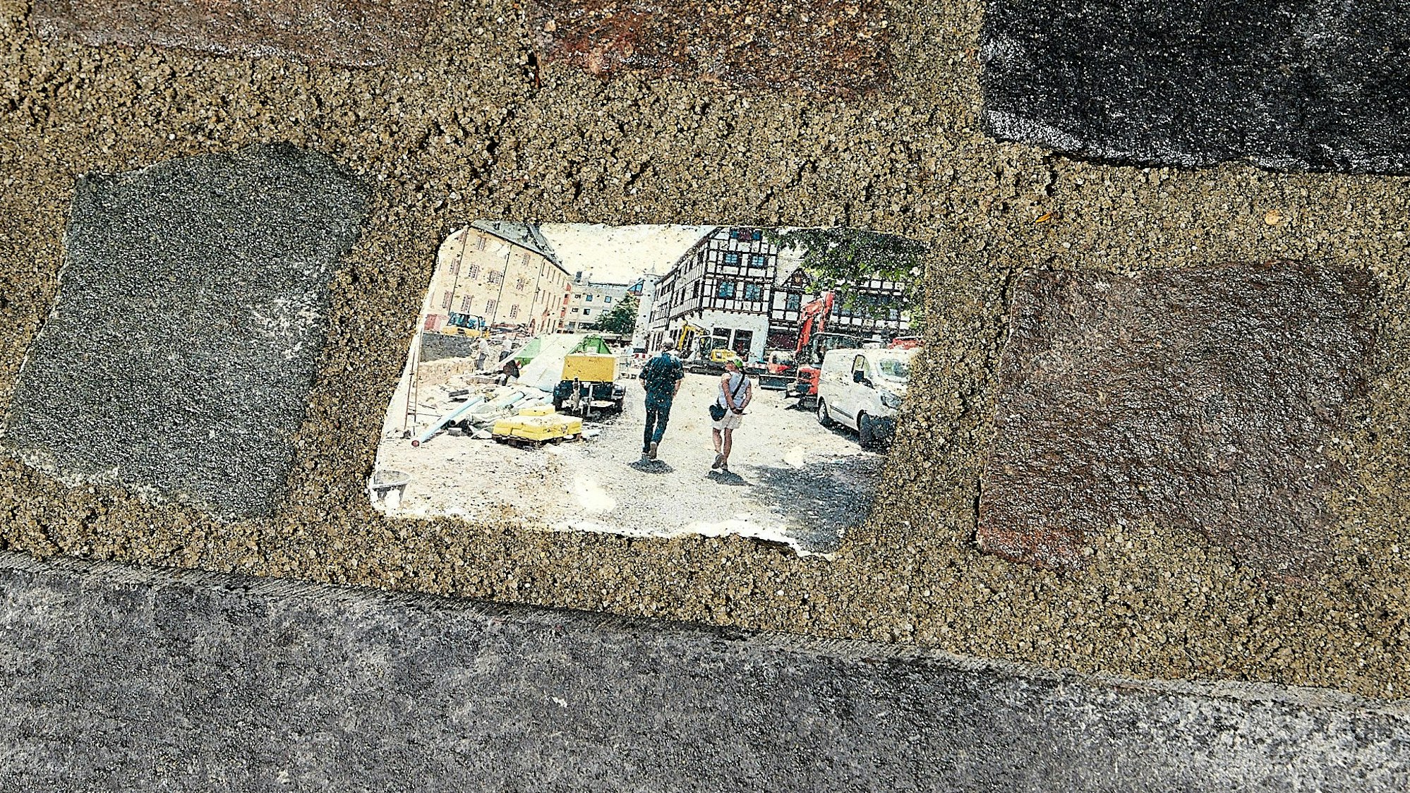 Das Bild zeigt mehrere einbetonierte Steine. Auf einem ist ein Motiv aus den Tagen nach der Flutkatastrophe in Bad Münstereifel aufgedruckt.