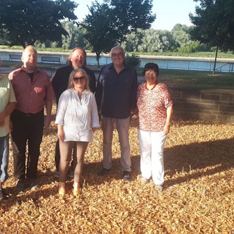 Vier Männer und zwei Frauen stehen unter einem Baum, im Hintergrund ist der Rhein zu sehen.
