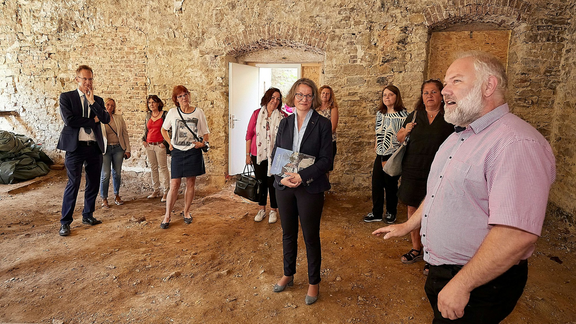 Eine Menschengruppe steht in einem Raum mit nackten Bruchsteinwänden und Lehmboden. Bernhard Ohlert (r.) erklärt die Besonderheiten der einstigen Brauerei.