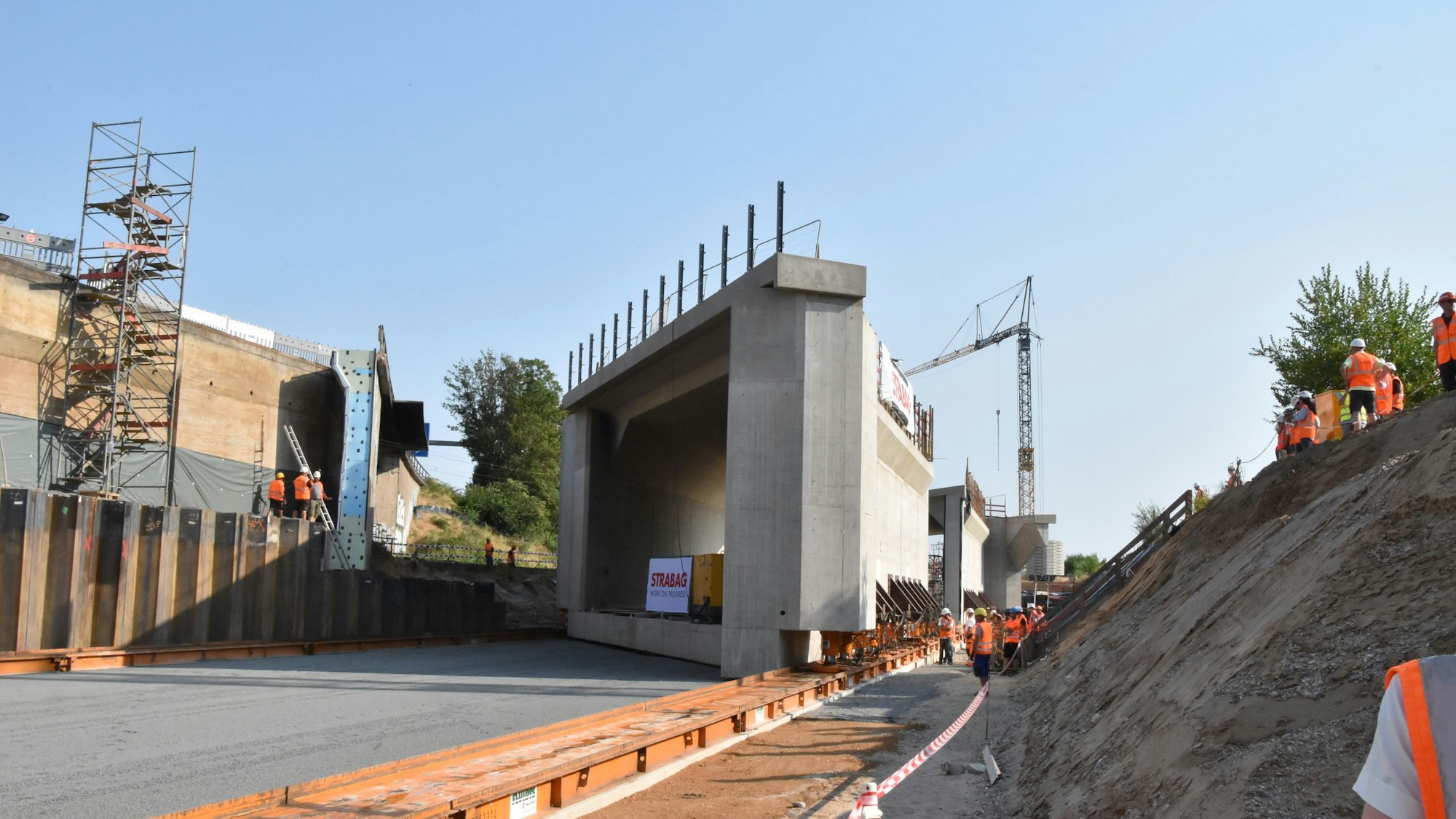 Die 9000 Tonnen schweren Brückenteile schweben auf orangefarbenen Schienen Richtung Süden.