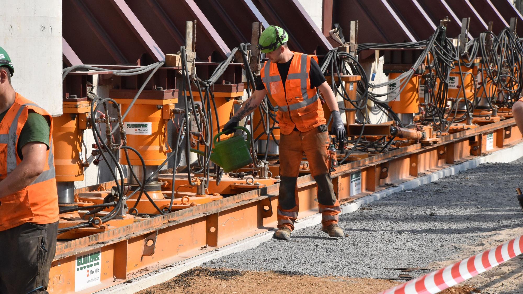 Der Mitarbeiter einer Baufirma ölt die Fläche, über die die horizontalen Hydraulikpressen die schweren Brückenteile schieben.