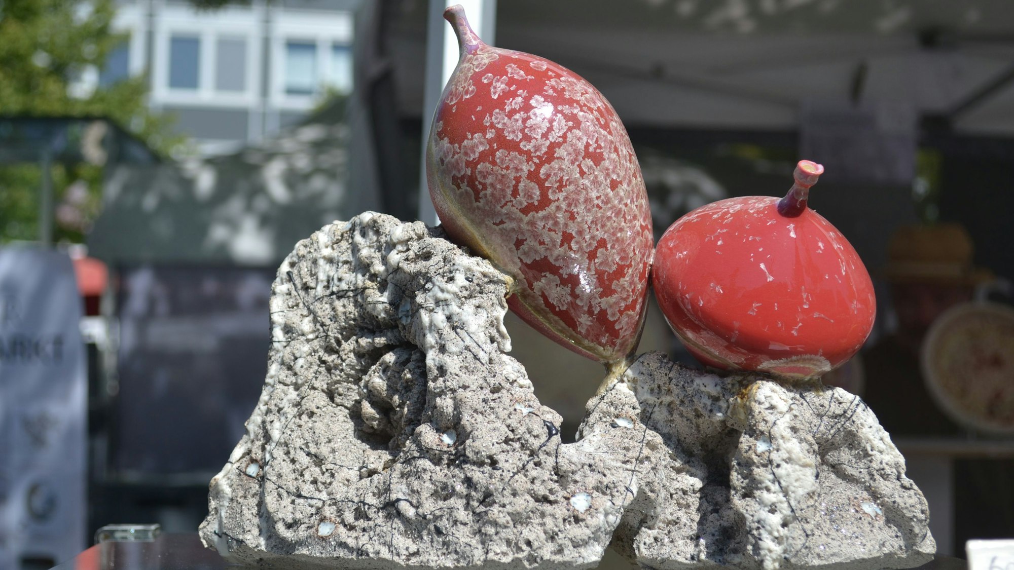 Auf einem grauen, rauen Stein liegen zwei glatte, rote Objekte, die in ihrer runden Form mit Stiel an Obst erinnern.
