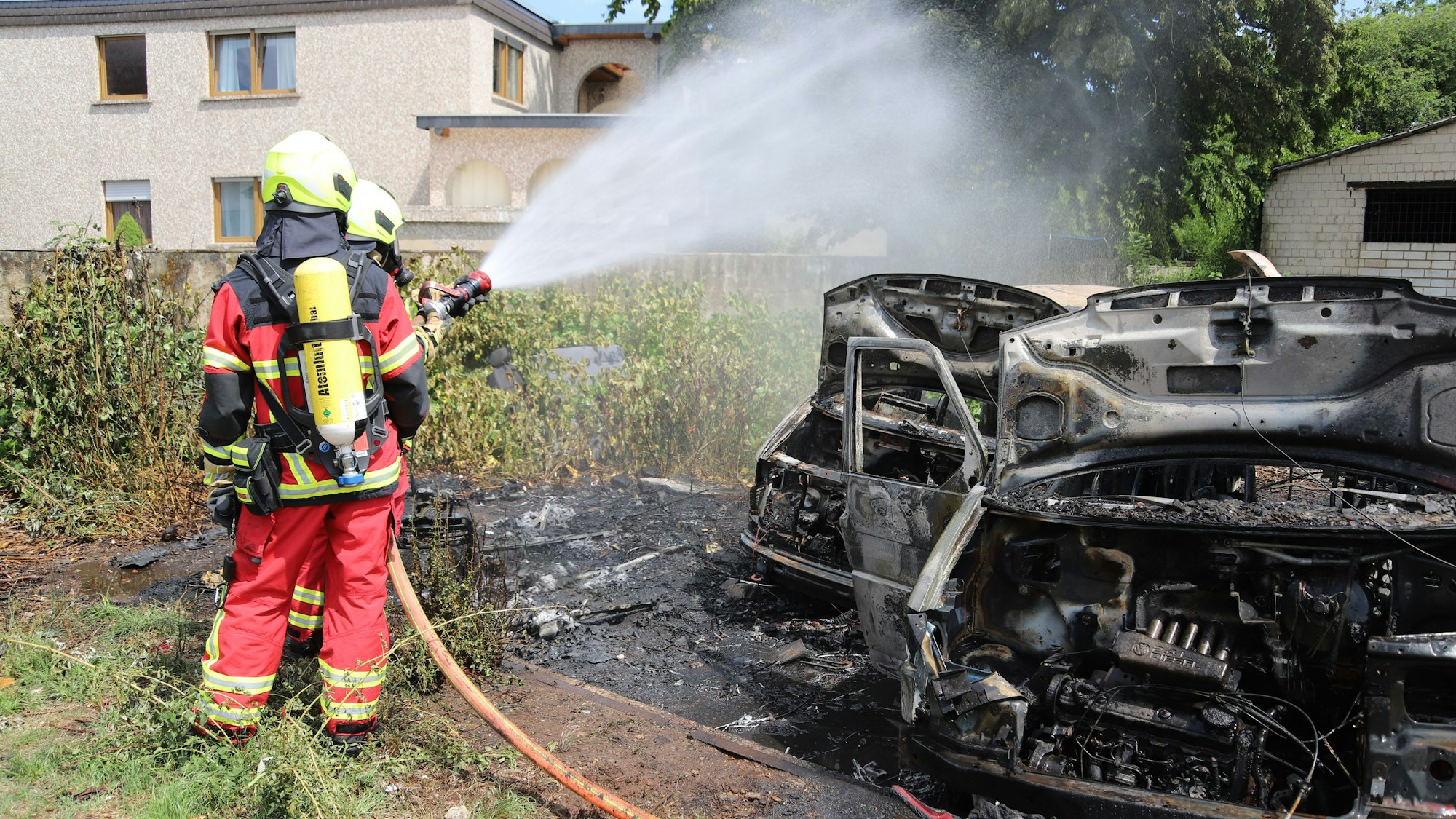 Feuerwehrleute löschen ein qualmendes Autowrack.
