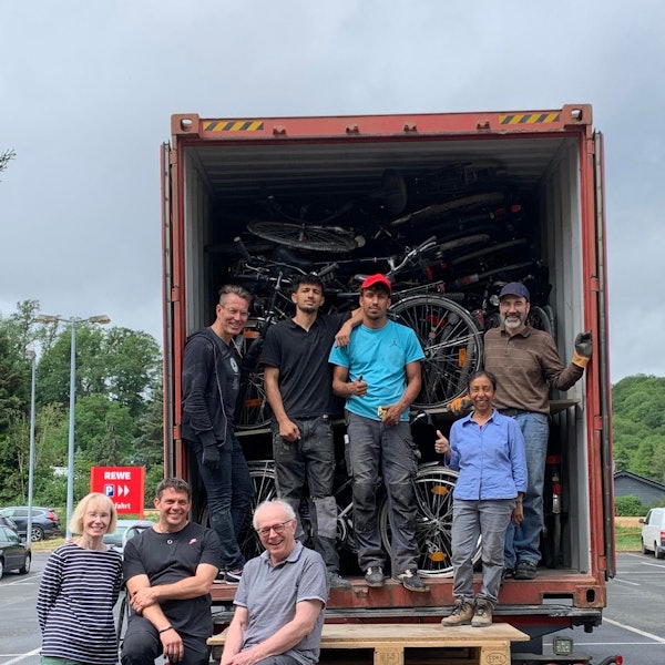 Eine Gruppe von Menschen steht vor einem mit Fahrrädern voll beladenem Container.