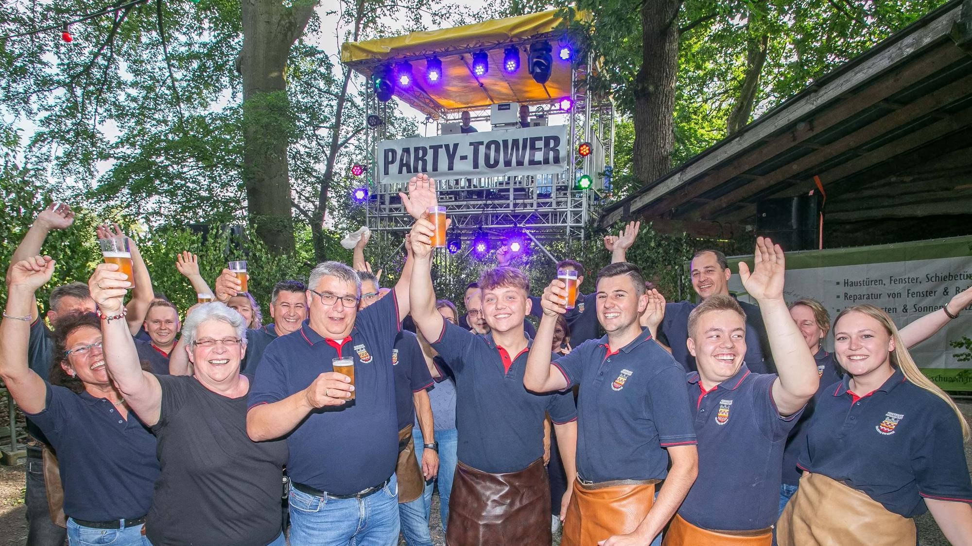 Mitglieder des Löschzugs Dörspetal der Bergneustädter Feuerwehr feiern ausgelassen unter dem Party-Tower. Und der steht mitten im Wald bei Pustenbach.