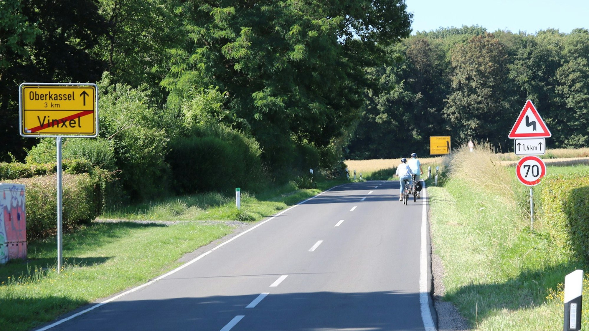 Zwei Radfahrer befahren die Landesstraße 490 bei Vinxel. Am linken Straßenrand steht ein Ortsausgangsschild.
