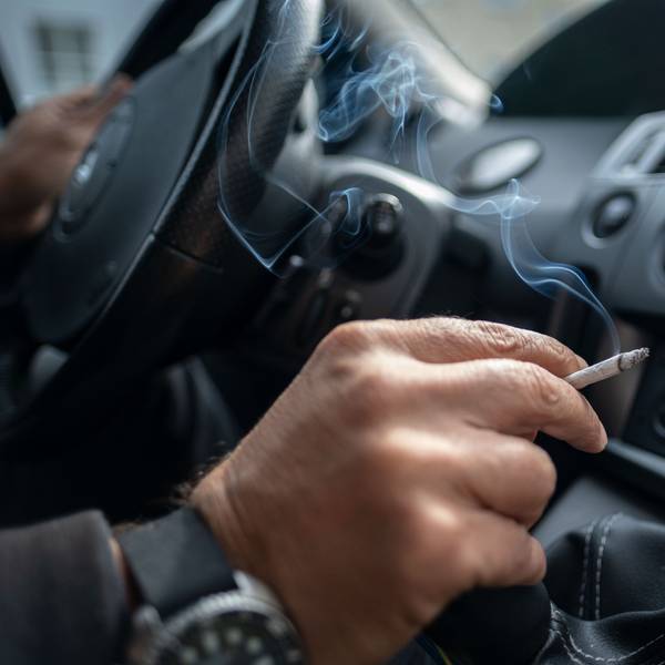 Ein Mann sitzt rauchend am Lenkrad eines Autos.