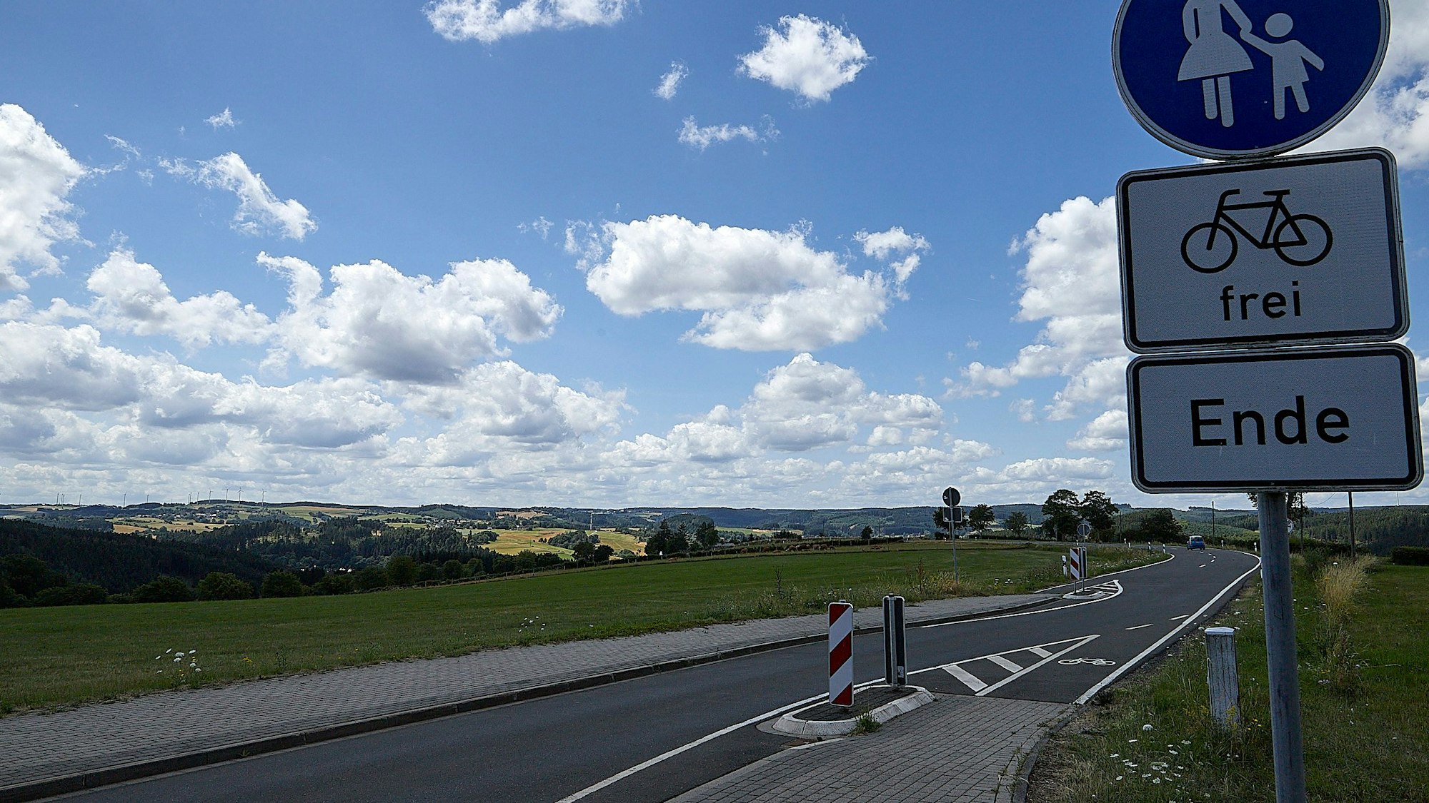 Blick in eine sommerliche Eifellandschaft. Im Vordergrund verläuft eine Straße mit Radweg.