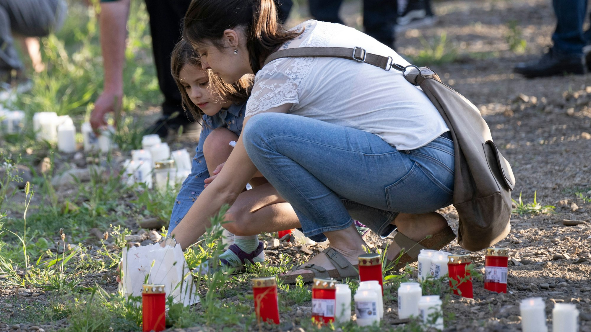 Zum Gedenken an die Todesopfer der Flutkatastrophe entzünden Menschen am Ufer der Ahr im Dorf Schuld Kerzen.