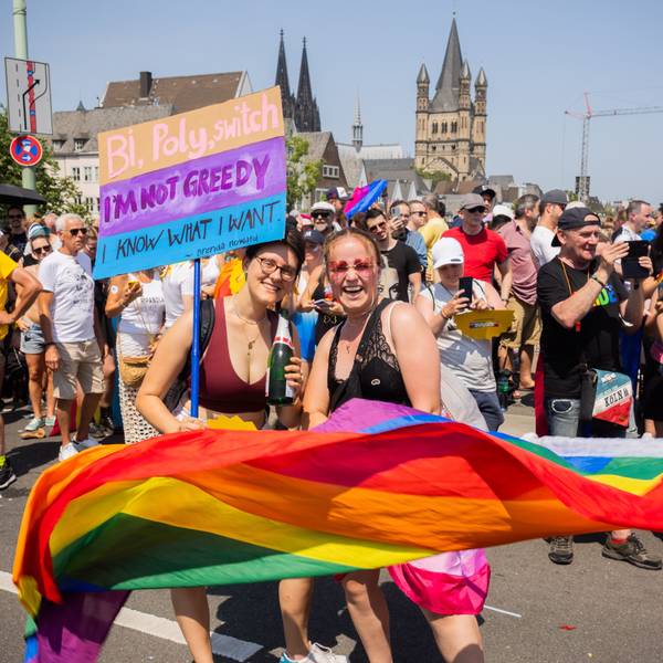 Bunt und politisch: der CSD 2023 lockte 1,4 Millionen Menschen an. Zwei Frauen schwenken eine Regenbogenfahne und werden von Zuschauenden fotografiert.