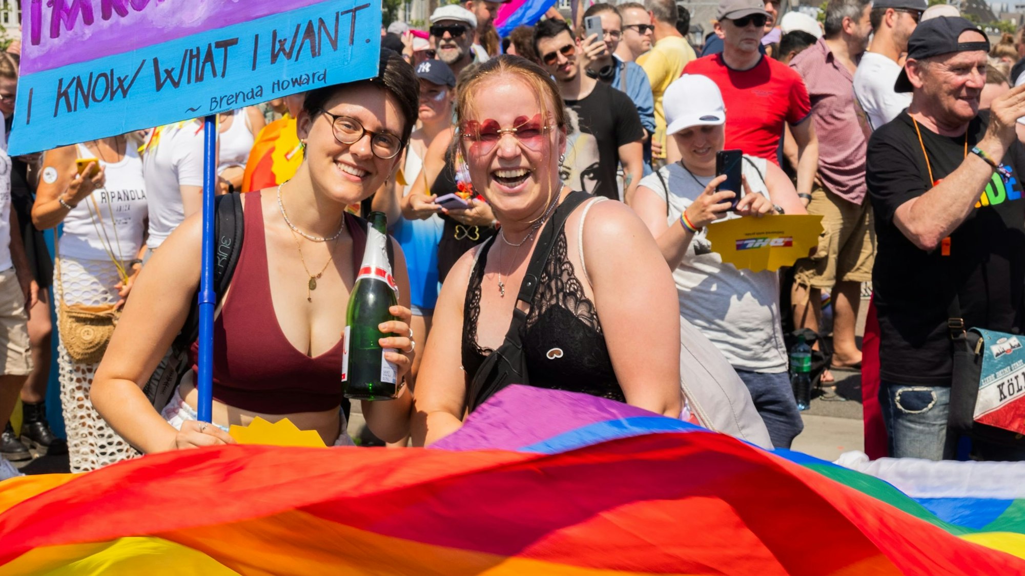 Bunt und politisch: der CSD 2023 lockte 1,4 Millionen Menschen an. Zwei Frauen schwenken eine Regenbogenfahne und werden von Zuschauenden fotografiert.
