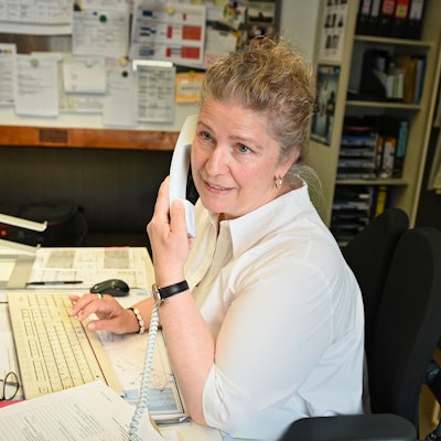 Sabine Döring
sitzt an einem Schreibtisch, mit der einen Hand tippt sie auf eine Tastatur und mit der anderen hält sie einen Telefonhörer.