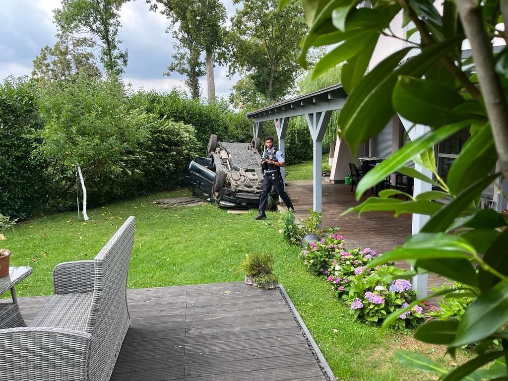 Ein Auto liegt in einem Garten auf dem Dach. Ein Polizist läuft umher.