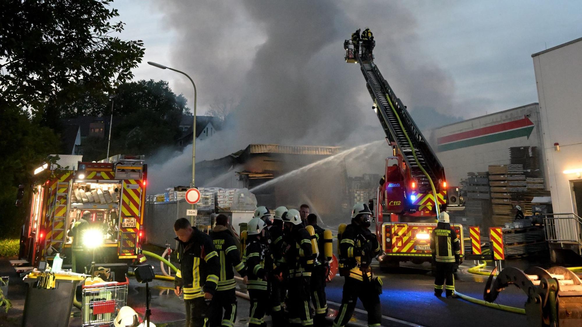 Viele Feuerwehrleute stehen zwischen zwei Feuerwehrwagen und schließen Löschschläuche an.