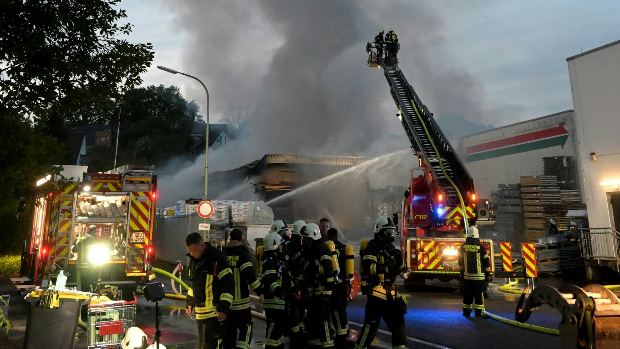 Viele Feuerwehrleute stehen zwischen zwei Feuerwehrwagen und schließen Löschschläuche an.