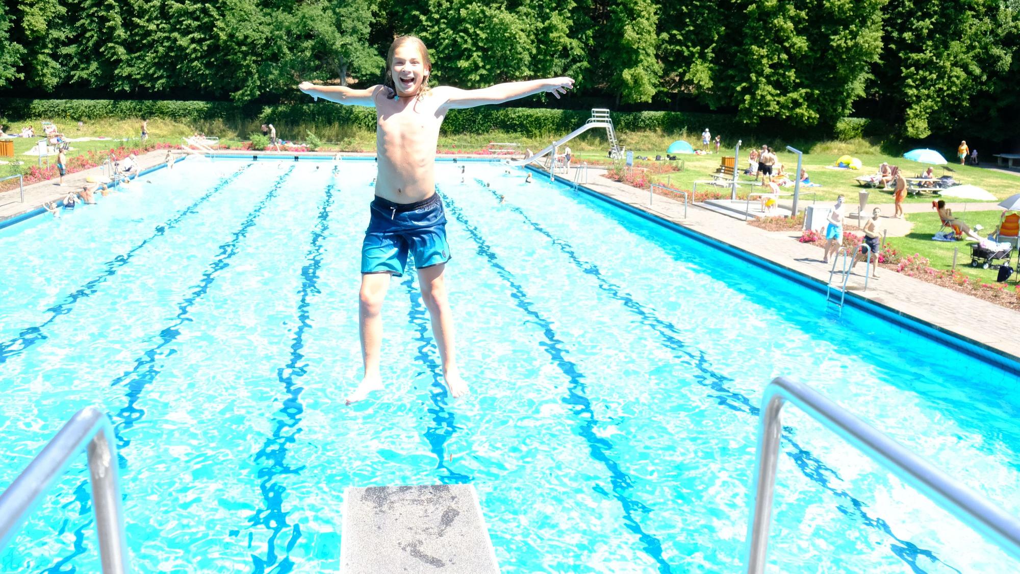 Ein Junge springt rückwärts vom Drei-Meter-Brett, im Hintergrund ist das Schwimmbecken zu sehen.