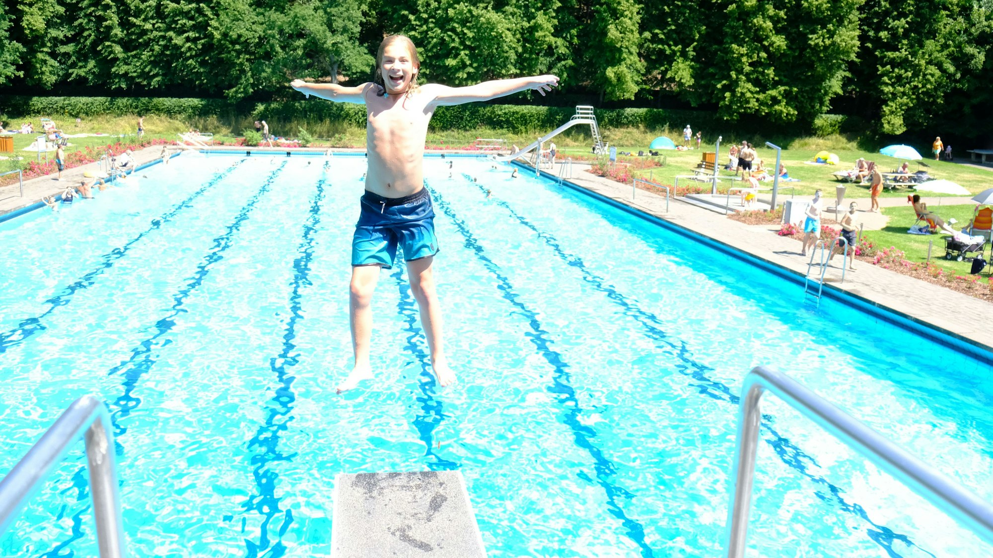 Ein Junge springt rückwärts vom Drei-Meter-Brett, im Hintergrund ist das Schwimmbecken zu sehen.