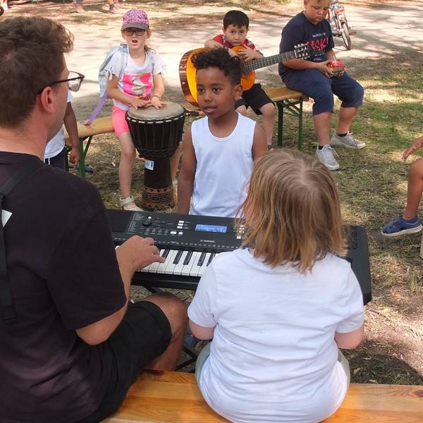 Kinder stehen und sitzen um einen Mann, der auf einem Keyboard spielt.