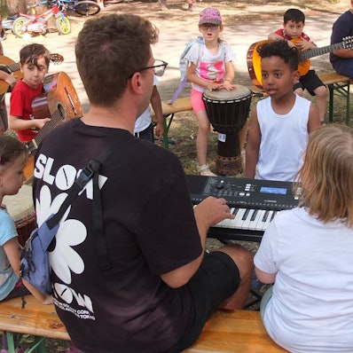 Kinder stehen und sitzen um einen Mann, der auf einem Keyboard spielt.
