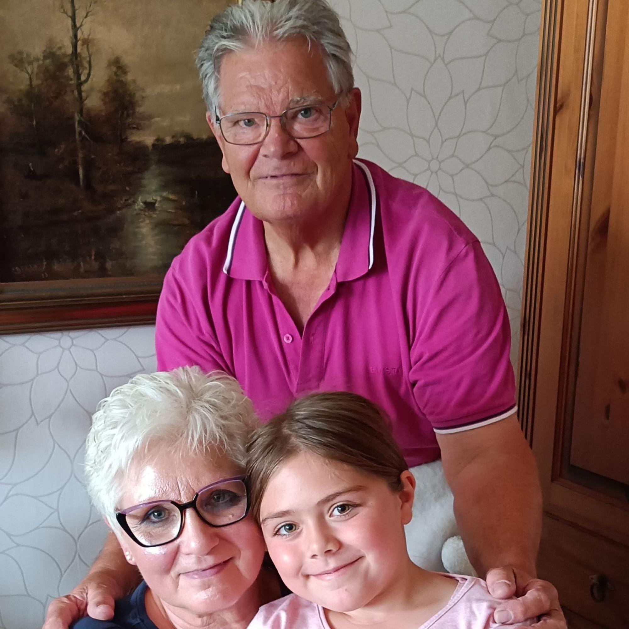 Josef und Agnes Pempe in ihrem Wohnzimmer. Agnes hat Enkelin Anna auf dem Schoß, Josef steht hinter beiden und hat die Hände auf ihren Schultern.